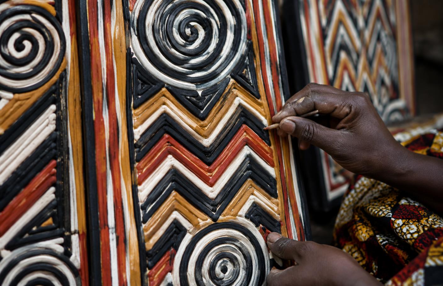 Artisan finishing raised geometric Imigongo panels in black, white, ochre and red