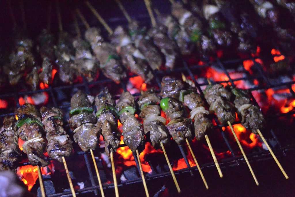 Brochettes on a charcoal grill under string lights at a Kigali bar